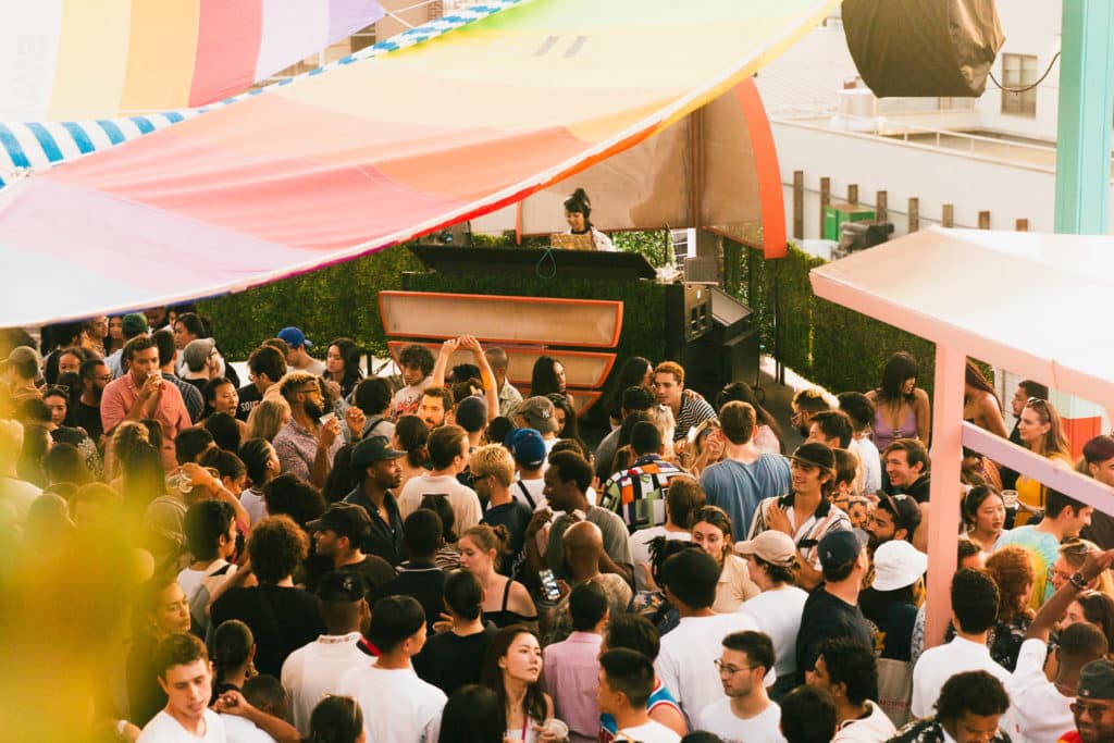The Elsewhere venue is shown with a dj in the back and crowd in front. Colorful drapes hang over the venue.