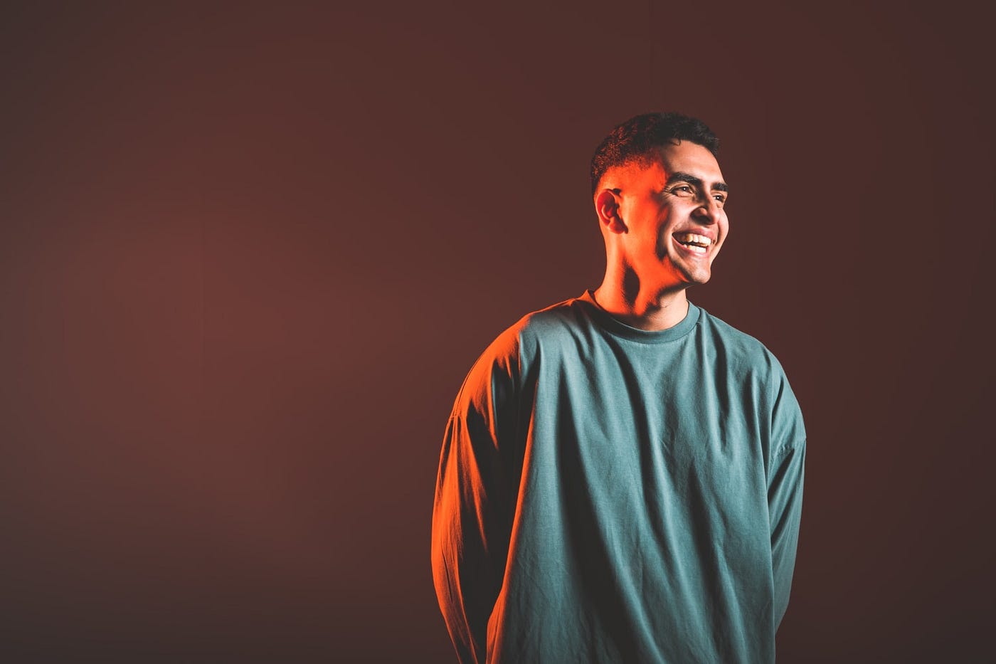 Sammy virji is shown smiling wearing a green crewneck with red lighting on his face and in the background.