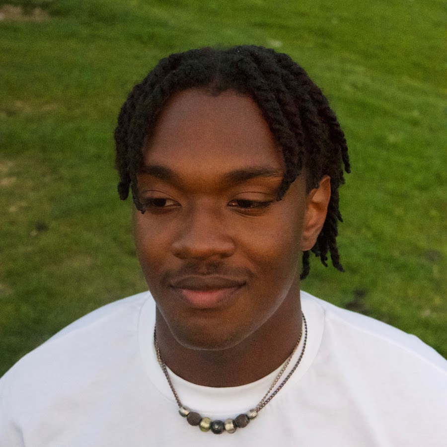 sondae is shown smiling in a white shirt and beaded necklace on a grassy background.