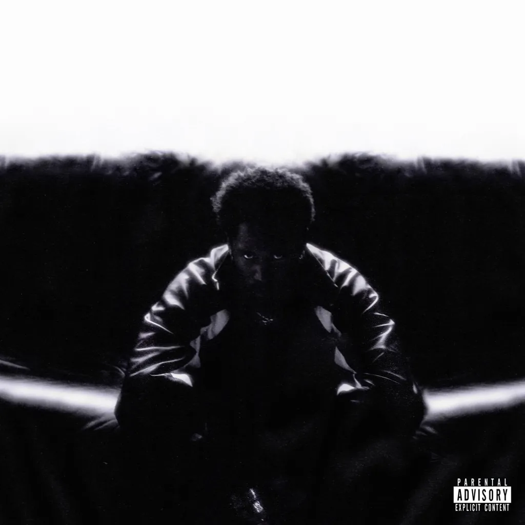 the cover for KAYTRANADA's Timeless album shows KAYTRANADA in all black in front of a black background with a white sky above him, leaning forward in a sitting position and looking intently forward.